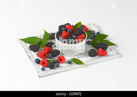 Frische Heidelbeeren, Brombeeren und Himbeeren in Schüssel geben und auf Holzbrett Stockfoto