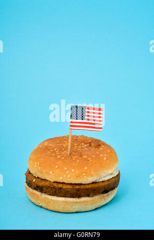 eine kleine Flagge der Vereinigten Staaten stecken in einen Hamburger auf blauem Grund Stockfoto