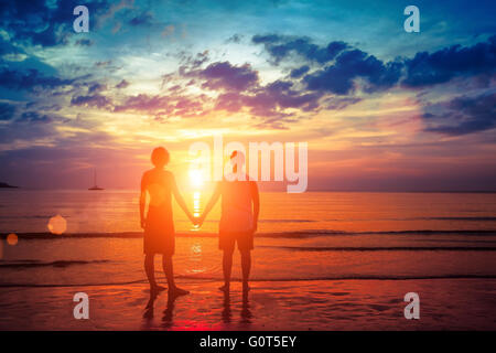 Junges Paar Liebhaber stehen hand in Hand am Strand bei Sonnenuntergang. Stockfoto