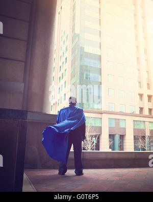 A business man wearing a super cape is standing in a city for a success, strength or power career concept. Stockfoto