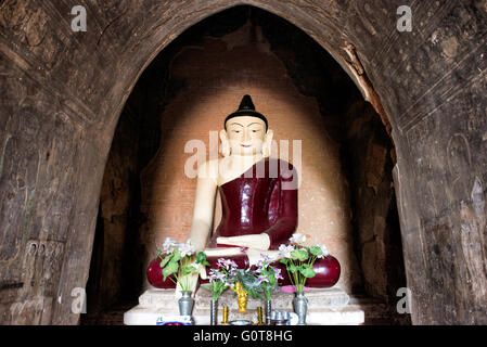 Tayok Pye Tempel Buddha Statue Bagan Myanmar // BAGAN, Myanmar - Eine große Buddha Statue in einem tiefroten Gewand befindet sich im Hauptschrein des Tayok Pye Tempels, umgeben von gut erhaltenen Fresken, die die Wände und die Decke der bogenförmigen Kammer bedecken. Der Tayok Pye Tempel stammt aus der Regierungszeit von König Narathihapate (1256–1287) und befindet sich auf der östlichen Seite der archäologischen Zone Bagan nahe dem Dorf Minnanthu. Der Tempel stellt die letzte Phase der monumentalen Konstruktion dar, bevor die mongolischen Invasionen den Niedergang des heidnischen Königreichs auslösten. Das Gebäude ist mit aufwändig renoviertem Stuck ausgestattet Stockfoto