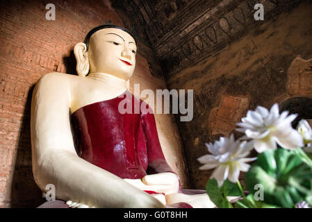 Tayok Pye Tempel Buddha Statue Bagan Myanmar // BAGAN, Myanmar - Eine große Buddha Statue in einem tiefroten Gewand befindet sich im Hauptschrein des Tayok Pye Tempels, umgeben von gut erhaltenen Fresken, die die Wände und die Decke der bogenförmigen Kammer bedecken. Der Tayok Pye Tempel stammt aus der Regierungszeit von König Narathihapate (1256–1287) und befindet sich auf der östlichen Seite der archäologischen Zone Bagan nahe dem Dorf Minnanthu. Der Tempel stellt die letzte Phase der monumentalen Konstruktion dar, bevor die mongolischen Invasionen den Niedergang des heidnischen Königreichs auslösten. Das Gebäude ist mit aufwändig renoviertem Stuck ausgestattet Stockfoto