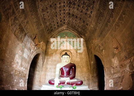 Tayok Pye Tempel Buddha Statue und Fresken Bagan Myanmar // BAGAN, Myanmar - Eine große Buddha Statue in einem tiefroten Gewand befindet sich im Hauptschrein des Tayok Pye Tempels, umgeben von gut erhaltenen Fresken, die die Wände und die Decke der bogenförmigen Kammer bedecken. Der Tayok Pye Tempel stammt aus der Regierungszeit von König Narathihapate (1256–1287) und befindet sich auf der östlichen Seite der archäologischen Zone Bagan nahe dem Dorf Minnanthu. Der Tempel stellt die letzte Phase der monumentalen Konstruktion dar, bevor die mongolischen Invasionen den Niedergang des heidnischen Königreichs auslösten. Die Struktur weist komplizierte Re Stockfoto