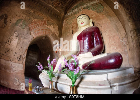 Tayok Pye Tempel Buddha Statue Bagan Myanmar // BAGAN, Myanmar - Eine große Buddha Statue in einem tiefroten Gewand befindet sich im Hauptschrein des Tayok Pye Tempels, umgeben von gut erhaltenen Fresken, die die Wände und die Decke der bogenförmigen Kammer bedecken. Der Tayok Pye Tempel stammt aus der Regierungszeit von König Narathihapate (1256–1287) und befindet sich auf der östlichen Seite der archäologischen Zone Bagan nahe dem Dorf Minnanthu. Der Tempel stellt die letzte Phase der monumentalen Konstruktion dar, bevor die mongolischen Invasionen den Niedergang des heidnischen Königreichs auslösten. Das Gebäude ist mit aufwändig renoviertem Stuck ausgestattet Stockfoto