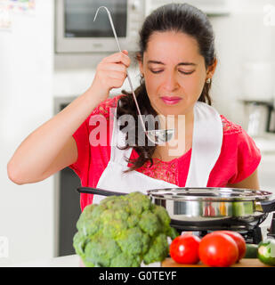 Junge Frau Koch schmeckendes Essen aus Kessel mit skeptischen Gesichtsausdruck Stockfoto