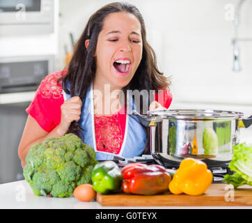 Junge Frau Koch Stand über Kessel kochen, ziehen ihr eigenes Haar in Frustration und verärgert Gesichtsausdruck mit Gemüse auf Schreibtisch Stockfoto