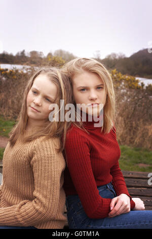 Zwei Schwestern sitzen Rücken an Rücken im freien Stockfoto