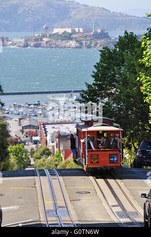 San Francisco, Vereinigte Staaten von Amerika, USA: eine Seilbahn auf Schienen im Hyde Street mit Alcatraz im Hintergrund Stockfoto