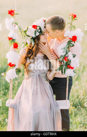 Gut aussehender Mann umarmt Rretty junge blonde tragen lila Kleid und Kranz in Gange sitzen Stockfoto