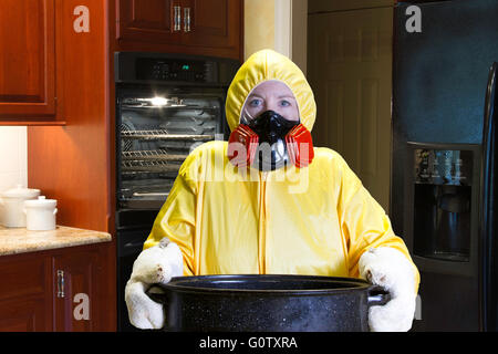 Frau in gelb Schutzanzug und Atemschutzmaske Holding Bräter in Küche. Stockfoto