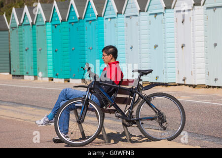 Bournemouth, Dorset, UK 5. Mai 2016. Mann sitzt auf der Bank mit Fahrrad durch Strandhütten auf Bournemouth promenade Credit: Carolyn Jenkins/Alamy Live News Stockfoto