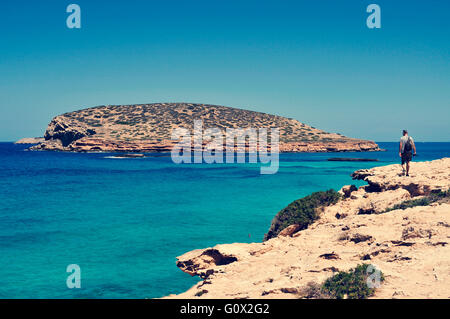 ein junger Tourist-Mann mit einer Kamera in der Hand geht neben dem Mittelmeer mit Blick auf die Insel Illa des Bosc, Isla Ibiza Stockfoto