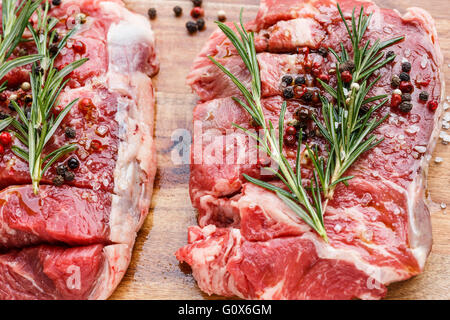 Rohes Rindfleisch-Steaks, Salz, Pfeffer, Rosmarin auf Schneidebrett Stockfoto