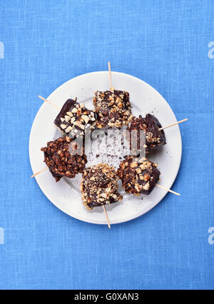 Sommer-Snack gefrorene Banane mit Schokolade und Nüssen auf blauem Hintergrund, Ansicht von oben bedeckt Stockfoto