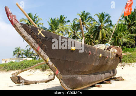 Holzboot steht am Rand des Strandes. Holzboot auf Hintergrund Flecken. Blick auf die Boote auf dem Hintergrund der Palmen Stockfoto