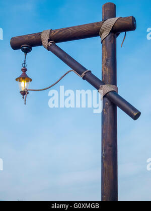 leuchtende Laterne auf einem Galgen-förmige hölzerne Struktur zusammengehalten durch Seile gegen den blauen Himmel in der frühen Abenddämmerung Stockfoto