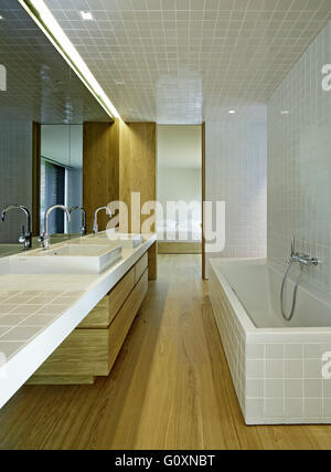 Schmale, modernes Bad mit weißen Fliesen und Wanne. Holzfußböden und Schränke. Stockfoto