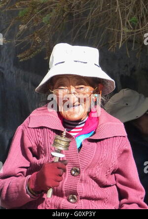 Tibetische alte Dame mit einem Handrad Gebet und singen von Mantras während auf ihrem Weg zum Kloster, ihre Gebete anzubieten. Stockfoto