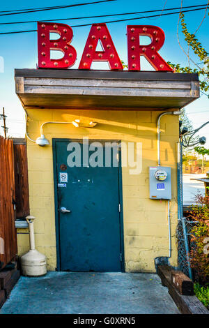 Eine niedrige Konzept industrielle Kante eine Hintertür Eingang zum Dive Bar mit einem riesigen roten Schild "BAR" am Dach scheint seltsam und arty Stockfoto