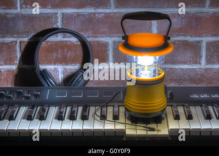 Leuchtende Hand Laterne stehend auf MIDI-Keyboard mit Kopfhörern auf dem Hintergrund der Ziegelwand, HDR-Verarbeitung Stockfoto