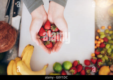 Draufsicht Nahaufnahme Schuss von einer Frauenhand mit frischen Erdbeeren über shopping Board mit Früchten. Halten Sie eine Handvoll o weiblich Stockfoto