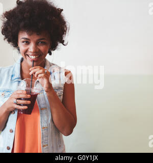 Porträt der glückliche junge Afrikanerin mit einem Saft aus frischen Früchten. Junge weibliche Modell Saft mit Strohhalm zu trinken. Stockfoto
