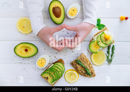 Hände machen Herzform mit Avocado belegte Brötchen Stockfoto