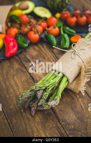 Reihe von frischem Spargel eingewickelt in Leinentuch mit Obst und Gemüse auf Holztisch Stockfoto