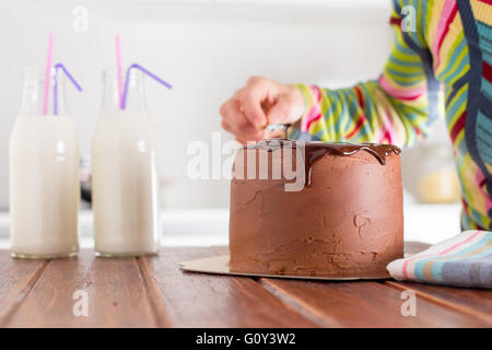 Frau einen Schokoladenkuchen mit Schokoladenglasur verzieren Stockfoto