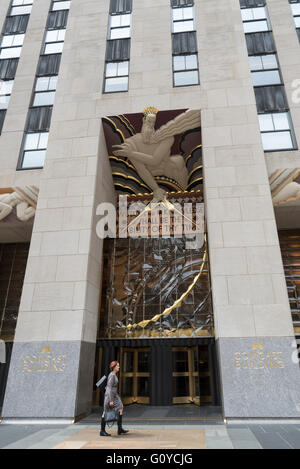 Frau zu Fuß hinter dem vorderen Eingang des Rockefeller Centers / Comcast Gebäude in New York City mit Art-déco-Relief Stockfoto