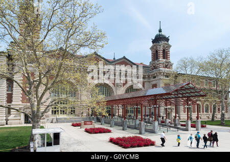 Vorderseite des Ellis Island Immigration Museum im Frühjahr, mit Touristen, Blumen und Bäume in voller Blüte. Stockfoto