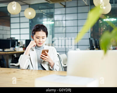 junge asiatische Büroangestellte mit Handy im Büro Stockfoto