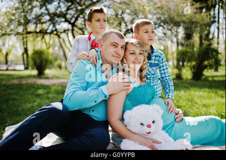 Glücklich schwanger paar mit zwei Söhnen umarmt und sitzen auf karierten Hintergrund Frühling Natur Stockfoto