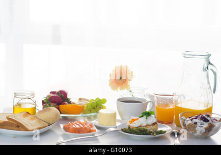 Frühstück vor dem Fenster mit Brei, pochiertes Ei, Lachs, Beeren, Früchte und Orangen Saft Stockfoto