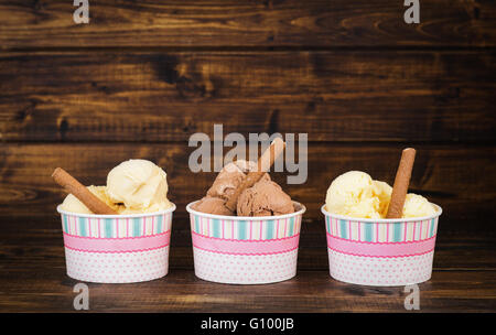 Drei verschiedene Arten von hausgemachtem Eis in Pappbechern auf dunklem Holz Stockfoto