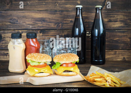 Zwei Cheeseburger mit zwei Flaschen Schwarzbier und zwei leere Becher auf hölzernen Hintergrund Stockfoto