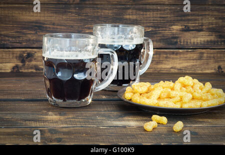 Zwei Becher mit Dunkelbier mit Erdnuss Puffs auf hölzernen Hintergrund Stockfoto