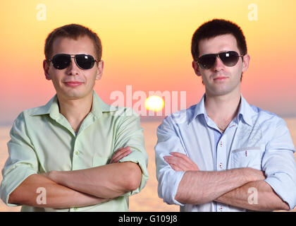 zwei Freunde bei Sonnenuntergang mit Sonnenbrille Falten ihre Arme Stockfoto