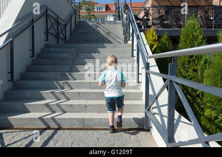 der kleine Junge in kurzen Hosen erhebt sich auf einer steilen Leiter Stockfoto