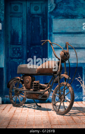 Zusammengesetztes Bild von einem rostigen Modell Motorrad aus Schrott vor blaue Tür gemacht. Stockfoto