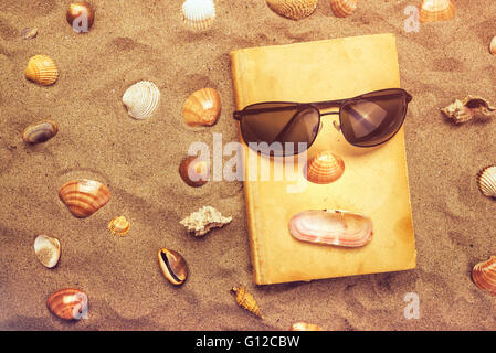 Lesen Sie alte Lieblingsbuch im Sommer Urlaub Strandurlaub, Draufsicht eines Buches und Sonnenbrillen in warmen Strand Schnee. Stockfoto