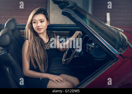 Attraktive Mädchen sitzen im klassischen amerikanischen Muscle-Car auf der Straße in der Nähe der alten Scheune abgestellt Stockfoto