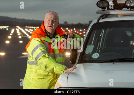 Bodenpersonal auf Start-und Landebahn am Flughafen Glasgow mit Landescheinwerfer im Hintergrund Stockfoto