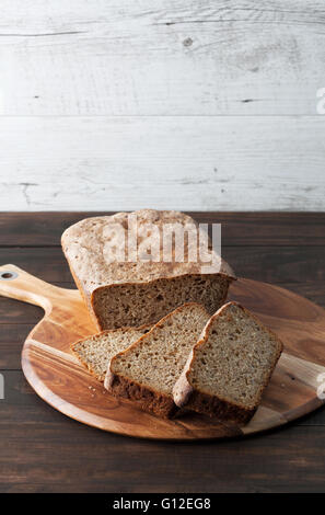 Hausgemachte dunkle Roggen Surdough Laib Brot und in Scheiben geschnitten auf Runde Schneidebrett. Vertikales Bild mit Textfreiraum. Stockfoto