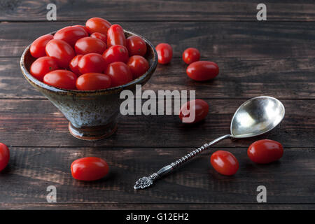 Cherry Tomaten Roma in Keramikschale auf Holztisch mit Vintage Löffel. Stockfoto
