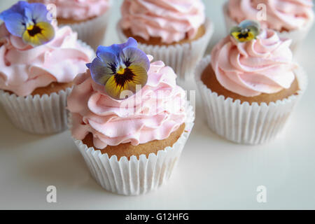 Hausgemachte rosa Zuckerguss Vanille Cupcakes mit essbaren Blüten Stockfoto