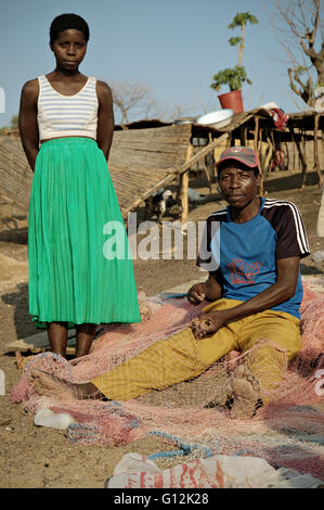 Fischer am Strand sitzen und Ausbessern von einem Fischernetz mit seiner Frau neben ihm stand, in dem Dorf Chembe, Malawi Stockfoto