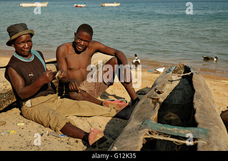 Zwei Männer sitzen am Strand am Ufer des Lake Malawi in Chembe Dorf, Cape Maclear Stockfoto
