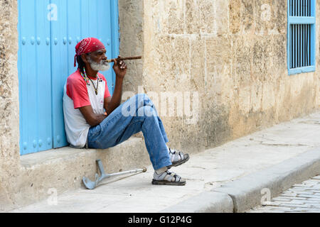 Ein älterer Mann sitzt auf einem Schritt einer großen Zigarre in Alt-Havanna, Havanna, Kuba Stockfoto