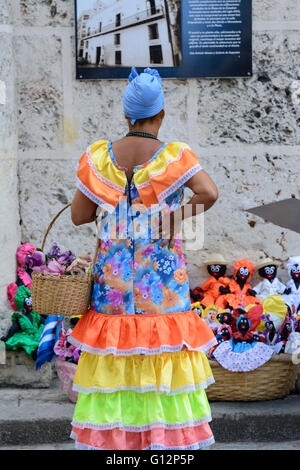 Eine Blumenverkäuferin tragen Tracht schaut Stoffpuppen auf Verkauf in der Plaza De La Catedral, Habana Vieja, Havanna, Kuba Stockfoto